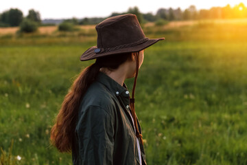 Obraz premium Defocus young woman in cowboy hat. Girl in a cowboy hat in a field. Sunset. Nature background. Woman looking in the direction of the sun. Hope, future. Out of focus