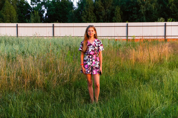 Defocus beautiful smiling teenage girl in dress standing against green summer background. High girl...