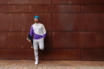 A young stylish man holds a skateboard. the man is leaning against the wall. Photo with copy space Urban background