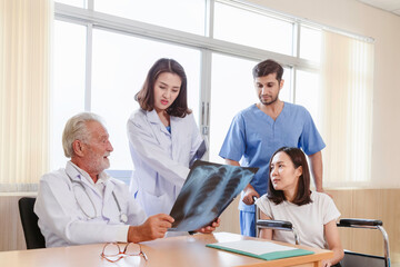 senior medical surgeon doctors showing female patient x-ray film to discuss and consulting with young female doctor and team before surgery at the hospital. healthcare and medical concept.
