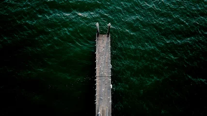 Tuinposter Top view of a wooden pier surrounded by dark green water © Collin Haag/Wirestock Creators