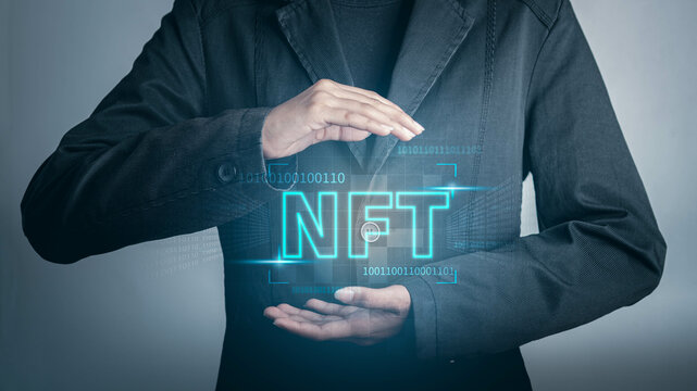 NFT non fungible tokens concept. Businessman holding digital unique art NFT text hologram on blue light