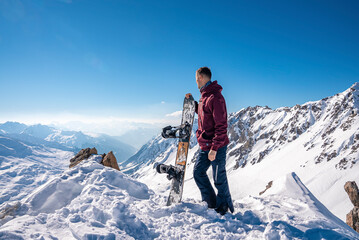 Fototapeta na wymiar St. Anton am Arlberg. March 10, 2022. Young man holding snowboard while standing on top of snowy mountain, Snowboarder stands on the background of beautiful view of snowcapped mountains
