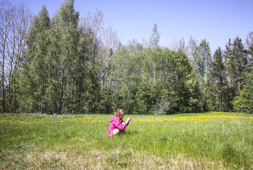 Little girl collects dandelion flowers on a spring meadow. 