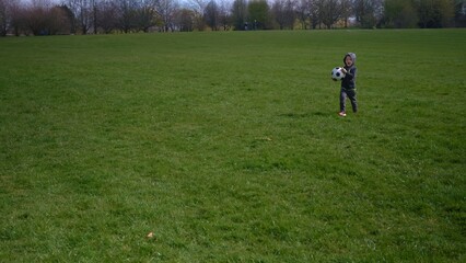 Happy Family Of Children Having Fun In Spring Park. Little Kid Run. Child Boy Dribbles Black White Classic Soccer Ball On Green Grass. People Playing Football. Childhood, Sport, Championship Concept