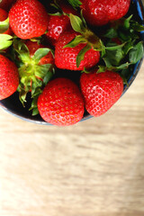 Bowl of fresh strawberries on wooden table, illuminated by sunlight. Flat lay.