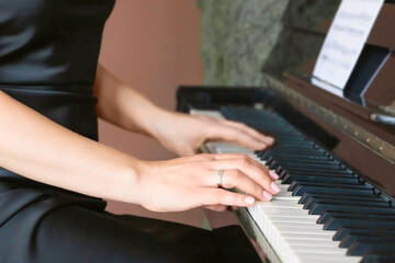 Obraz premium Selective focuse of hand of an adult woman with a beautiful manicure against the background of black and white keys of a classical piano. The concept of creative activities, hobbies.