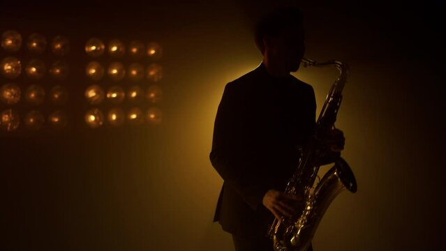 Silhouette man saxophonist playing instrument on stage. Guy playing sax in club.
