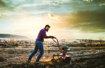 organic farming man cultivates the ground at sunset with a tiller  preparing the soil for sowing