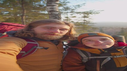 POV vertical shot of cheerful tourist couple standing on mountain top in winter, smiling and waving on camera while taking selfie and chatting on video call - Powered by Adobe