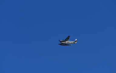 Floatplane, a type of seaplane with one or more slender floats mounted under the fuselage, photographed in flight against blue background