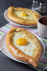 Khachapuri in Adjarian, Open pies with suluguni cheese and egg yolk in the form of boat on plates on gray background, Traditional Georgian cuisine