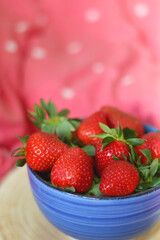 Bowl of fresh strawberries on a bed with colorful bedding. Selective focus.