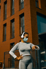 Fototapeta na wymiar Woman in light gray sportswear and medical mask having a break during training on the street
