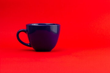 Side shot of a ceramic dark blue teacup on a red background.