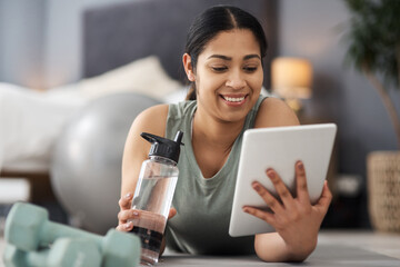 Just doing a bit of browsing. Shot of a sporty young woman using a digital tablet while exercising at home.