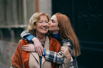 A happy grandmother and granddaughter hugging and kissing outside. - 498599554