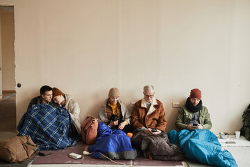 Minimal front view at diverse group of refugees hiding in shelter together during war or crisis,...