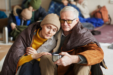 Front view portrait of Caucasian senior couple hiding in refugee shelter covered with blanket on...