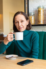 Woman holding cup of coffee near face. Pensive drinking tea, sitting in cafe.