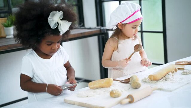 Diverse group of African American and Caucasian girls prepare the dough and bake cookies in the kitchen while learning in the class at school