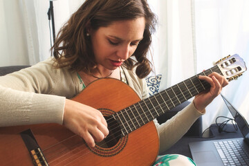 Attractive young lady playing and recording music using a Spanish classical guitar and a laptop