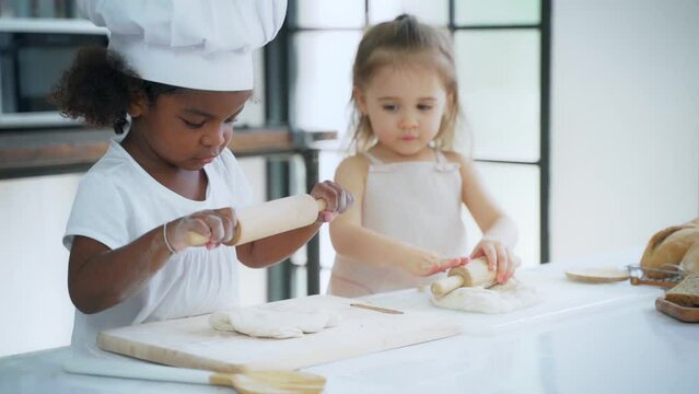 Diverse group of African American and Caucasian girls prepare the dough and bake cookies in the kitchen while learning in the class at school