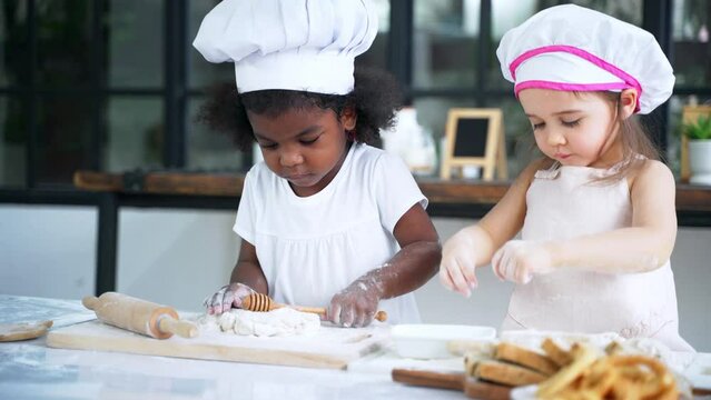Diverse group of African American and Caucasian girls prepare the dough and bake cookies in the kitchen while learning in the class at school