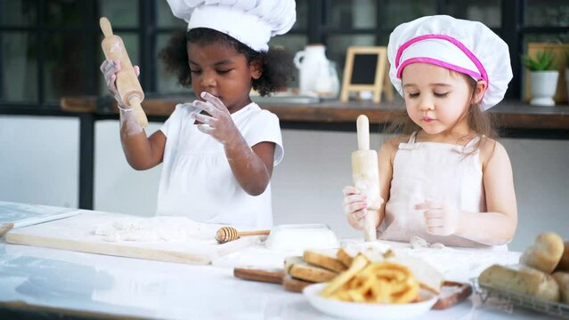 Diverse group of African American and Caucasian girls prepare the dough and bake cookies in the kitchen while learning in the class at school