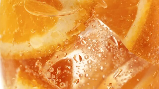Orange pieces with ice cubes and fizzy carbonated water bubbles in glass summer cocktail drink macro