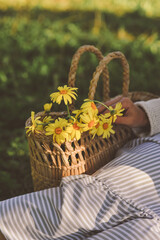 Woman sitting near straw bag with yellow daisies in the park on summer day. Summer concept