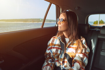Stylish young woman sitting on back seat in the taxi car and looking through the window