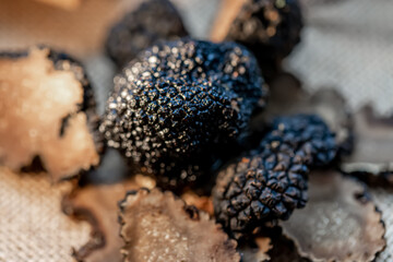 Soft focus of truffles on the surface.Thinly sliced mushrooms. Black raw champignons on a beige burlap. Top view. Dark background. Shallow depth of field.The artistic intend and the filters.