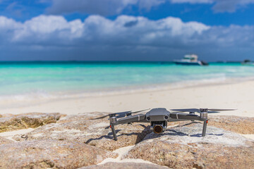 Drone landed on rocks surface next to seashore. Blurred tropical beach shore, coastline landscape, boats and cloudy sky. Luxury filming, footage and content creating for tourism, advertising