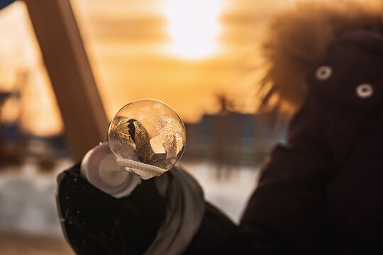 a girl holds a soap bubble with beautiful frost patterns in the rays of the sun in winter