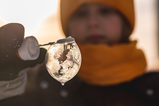 a girl holds a soap bubble with beautiful frost patterns in the rays of the sun in winter