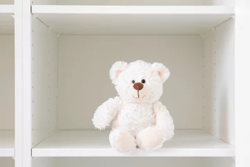Foto op Plexiglas Smiling white teddy bear sitting on shelf in wardrobe. Closeup. Front view. © fotoduets
