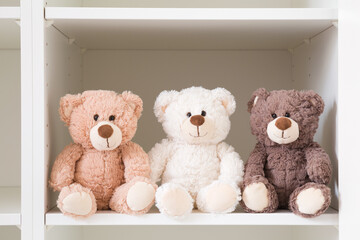 Smiling white, light brown and dark brown teddy bears sitting on shelf in wardrobe. Togetherness...