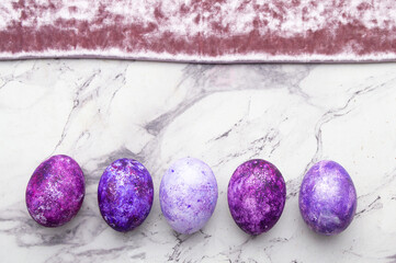 purple Easter eggs lie in a row on a marble background. A postcard with a place for the text.