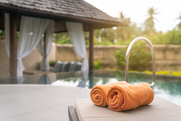 Folded orange towels on lounge chair by the  pool side, private pool villa, vacation