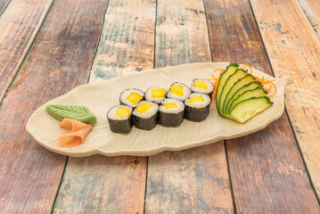 Maki portion stuffed with rice with Japanese vinegar and mango wrapped in nori seaweed and grated carrot, cucumber slices, ginger and wasabi in cream on a white sheet tray