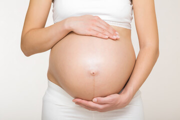 Young adult pregnant woman in white clothes touching big naked belly with hands. Showing shape....