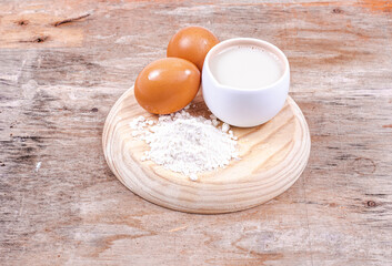 Wooden board with fresh eggs, flour and oat milk on a dark wooden background