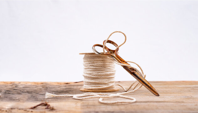 old rusty scissors resting on a spool of thread on a wooden table with a white background