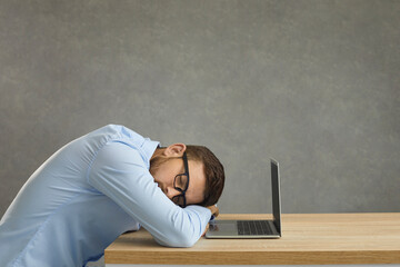 Tired college student, office worker or professional programmer sleeping lying down near laptop computer screen exhausted by tiresome study workload or overtime work overload. Copy space in background