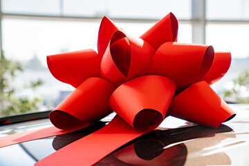 a red gift bow on the roof of a new black car in the car dealership. 