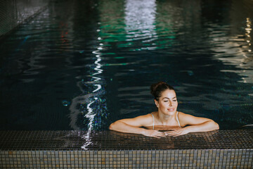 Young woman relaxing on the poolside of indoor swimming pool