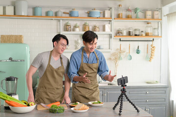 Young two close friend bloggers preparing food in the kitchen while live streaming via smartphone.