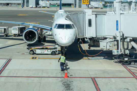 Man working on an airport runway putting a hitch on the front wheel of the plane