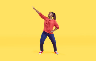Funny young African American woman isolated on yellow studio background dance in casual clothes. Smiling millennial black girl have fun make dancer moves enjoy celebration or party.